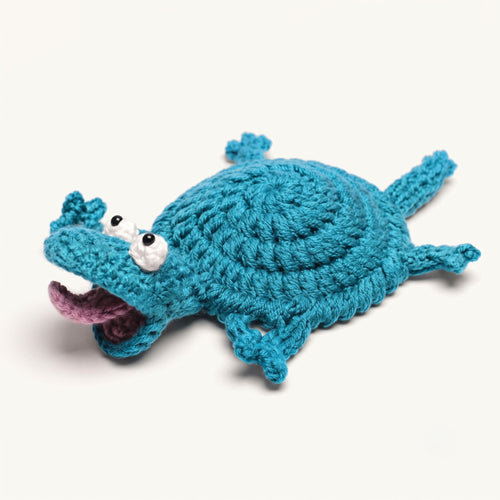 A crisp studio hero shot of the By1994 crochet lizard cup coaster in ocean blue, showing detailed handmade cotton knit loops, splayed gecko legs, and a whimsical open mouth with a pink tongue on a clean white background.