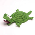 A top-down studio shot of the By1994 handmade crochet lizard drink coaster in sage green, featuring high-density organic cotton yarn craftsmanship and expressive white eyes lying flat on a light cream surface.
