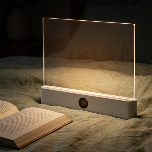 A serene close-up lifestyle image of the white flat page reading lamp standing upright on a textured green bed blanket next to an open book, casting a soft, warm localized glow in a dimly lit room.