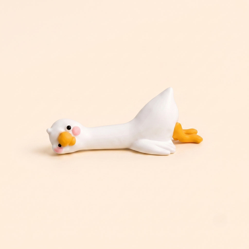 A minimalist studio product shot of the By1994 mini duck figurine in the Lying pose, showing a cute white resin duck resting flat on its belly against a light cream backdrop.