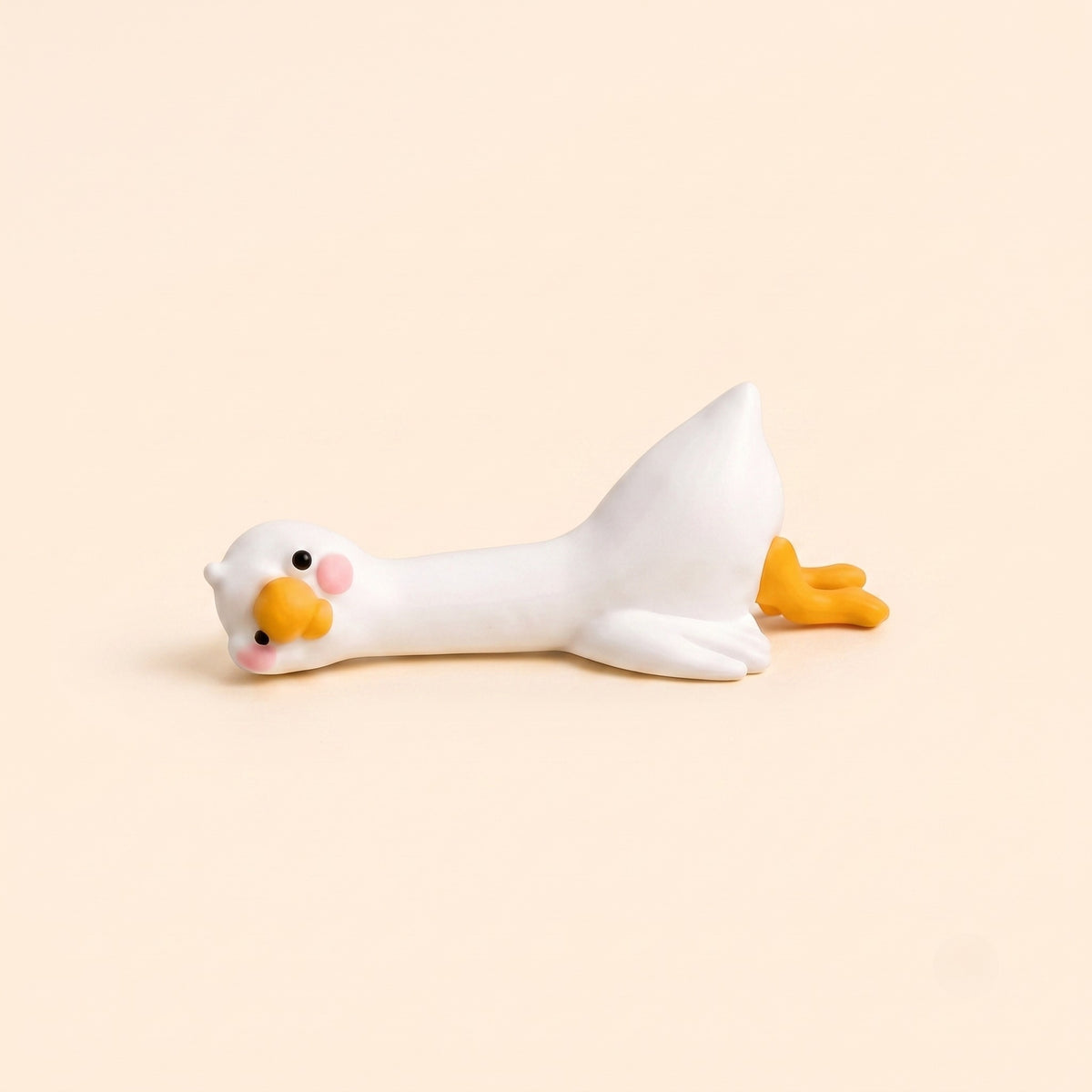 A minimalist studio product shot of the By1994 mini duck figurine in the Lying pose, showing a cute white resin duck resting flat on its belly against a light cream backdrop.