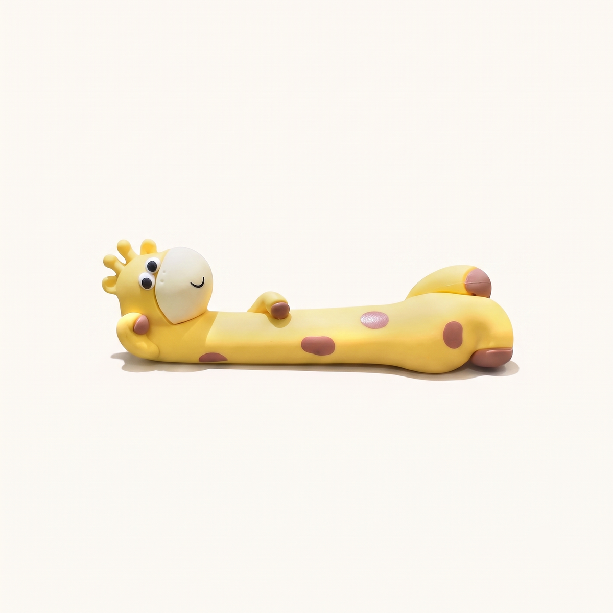 A studio hero shot of the By1994 mini giraffe figurine in a relaxed lying pose resting on its side, crafted from smooth matte yellow eco-resin with warm brown spots on an off-white background.