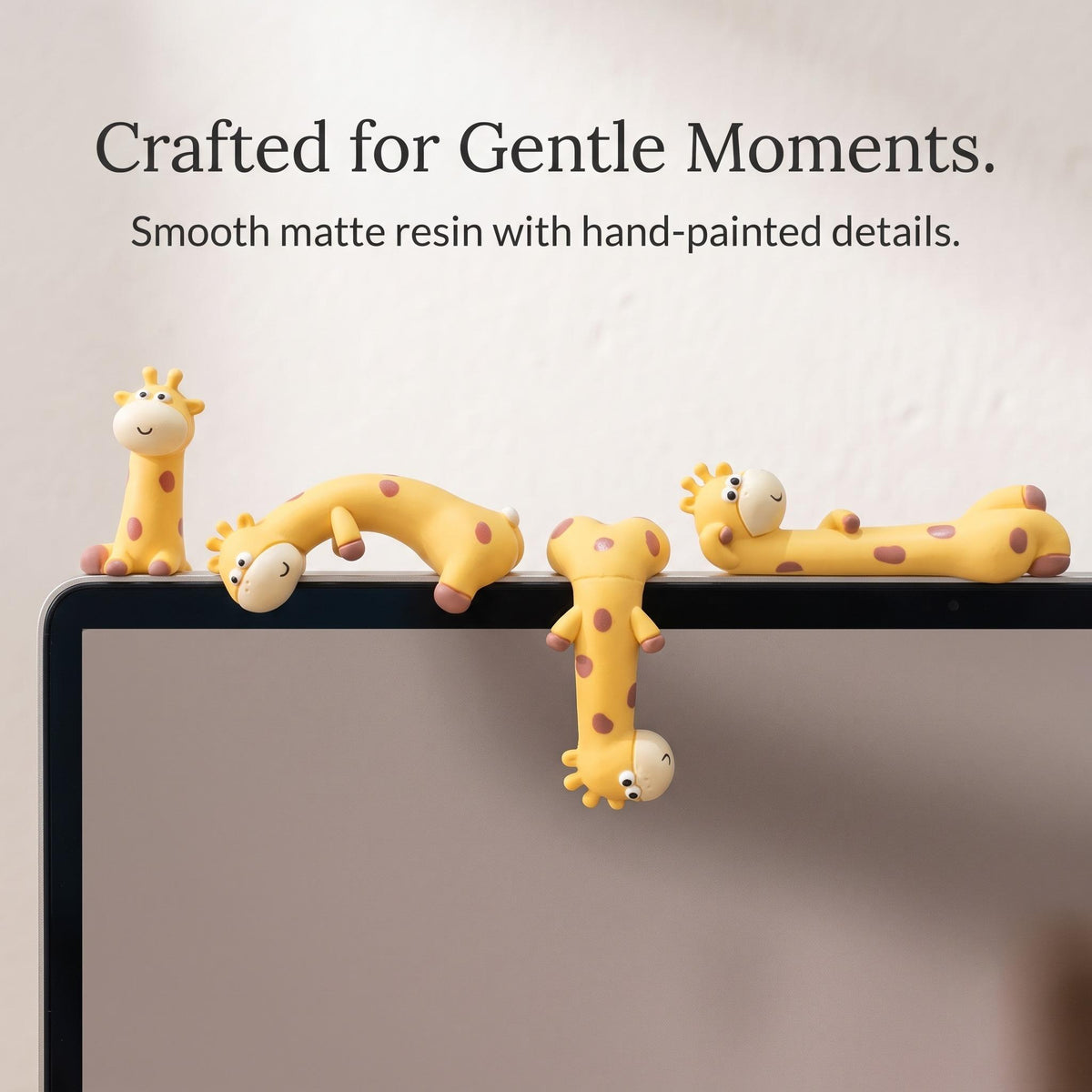 A close-up product lifestyle slide showing four mini giraffe figures balanced along the top edge of a computer screen, with text overlay reading Crafted for Gentle Moments. Smooth matte resin with hand-painted details.