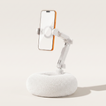 A crisp studio hero shot of the By1994 plush pillow phone holder in Ivory White, featuring a clean white mechanical arm holding a smartphone vertically on a light beige background.